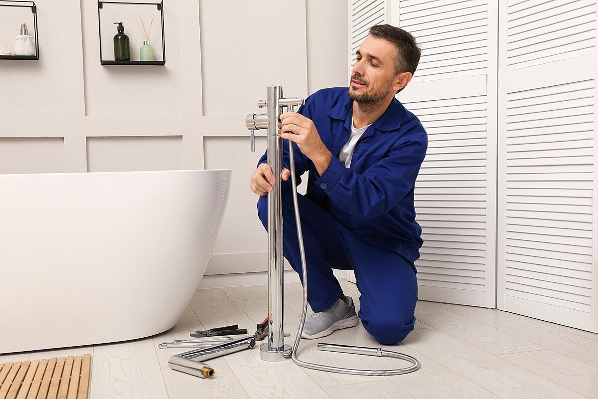 Plumber installing a chrome faucet beside a bathtub